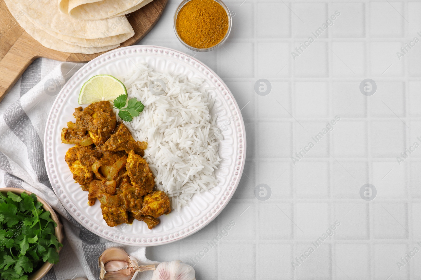 Photo of Delicious chicken curry with rice and ingredients on white tiled table, flat lay. Space for text