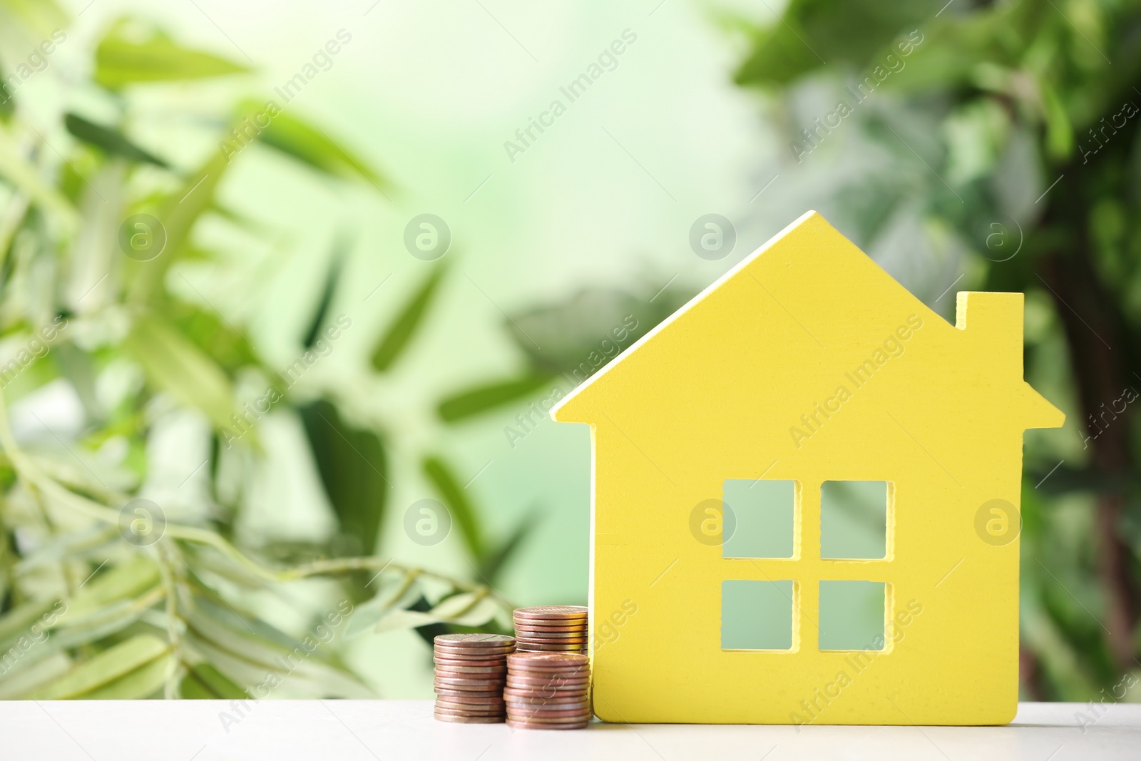 Photo of House figure and coins on table against blurred background. Space for text