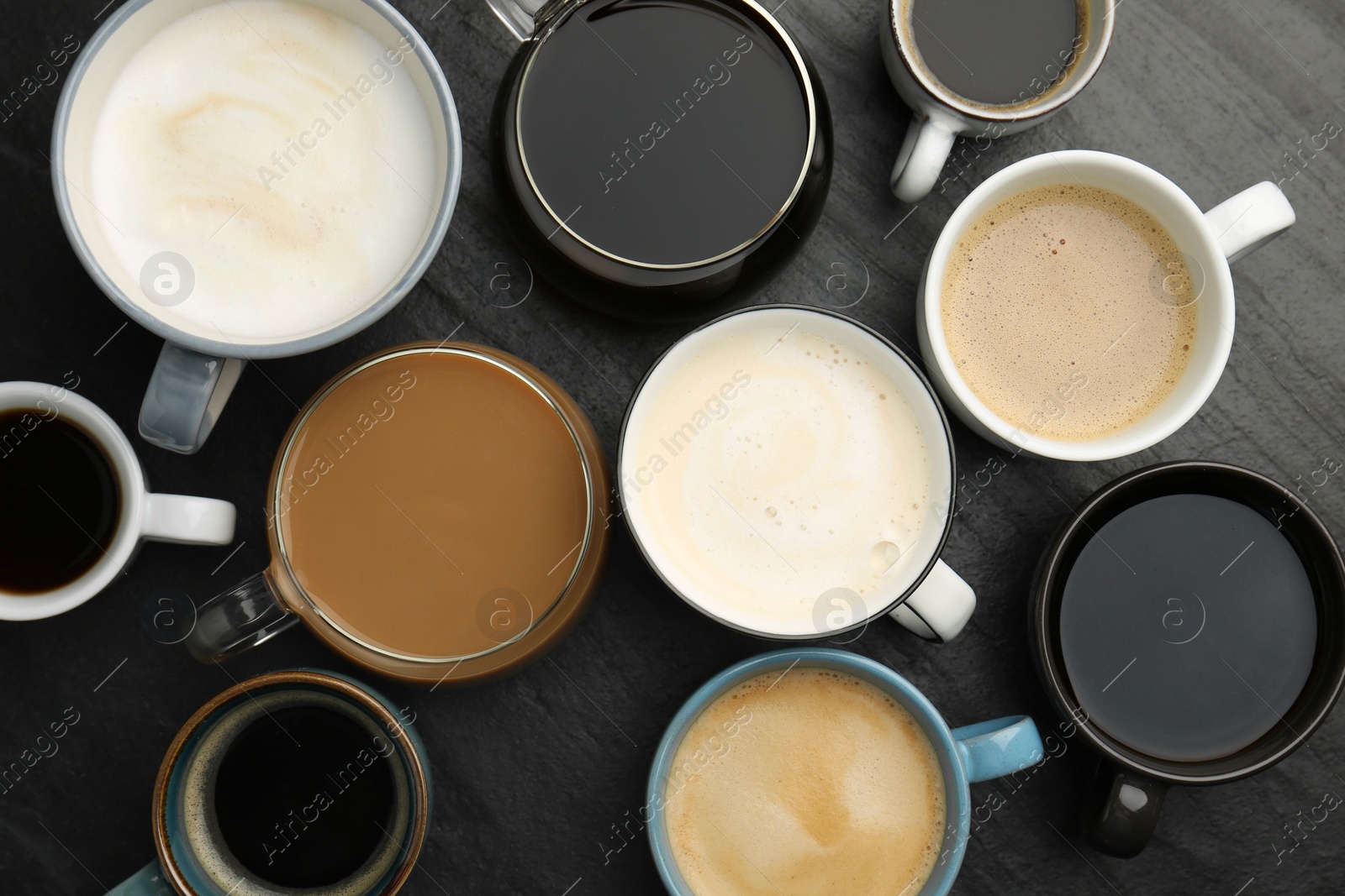 Photo of Different coffee drinks in cups on dark textured table, flat lay