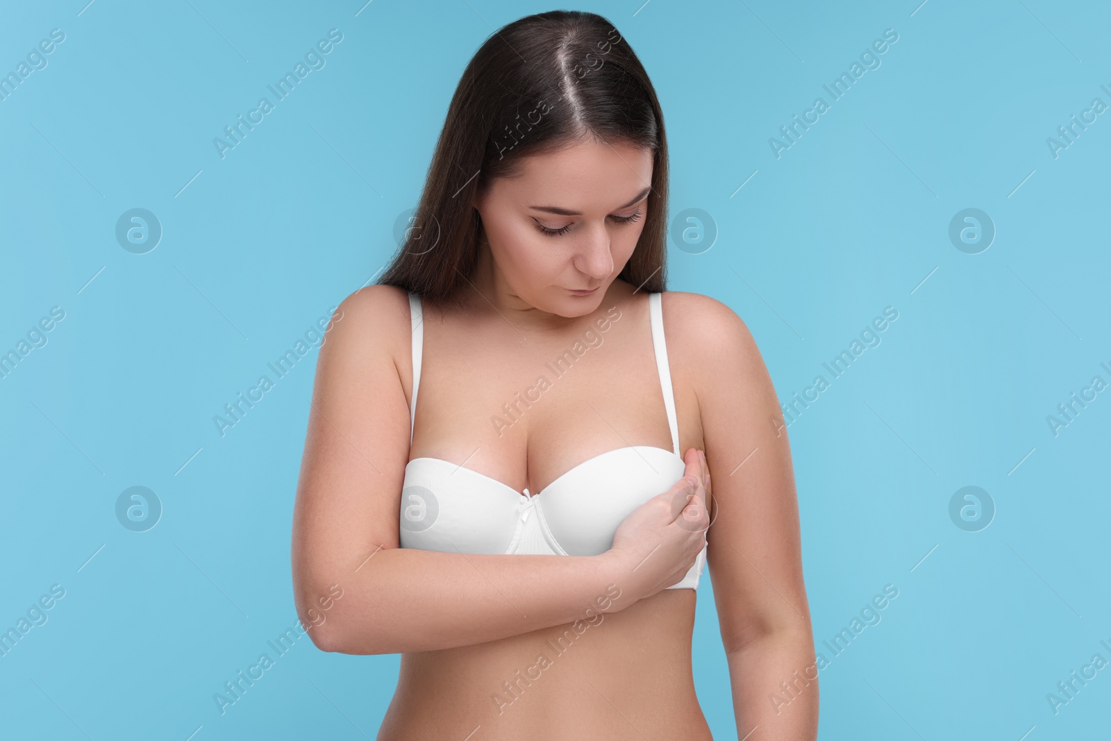 Photo of Mammology. Woman in bra doing breast self-examination on light blue background