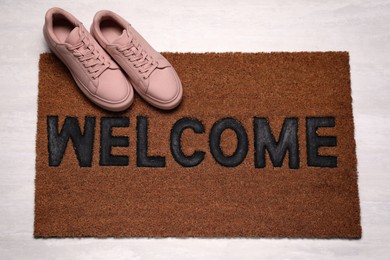 Photo of New clean mat with word WELCOME and shoes on floor, above view