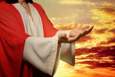 Image of Jesus Christ reaching out his hands and praying at sunset