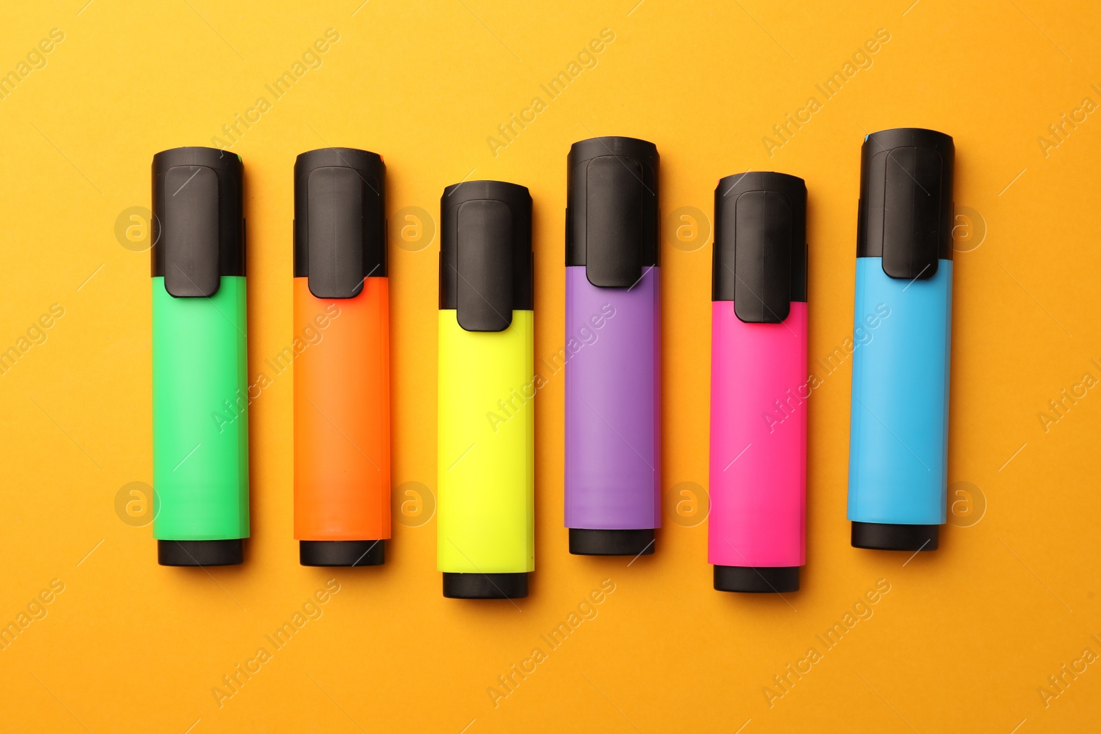 Photo of Bright markers on orange background, flat lay