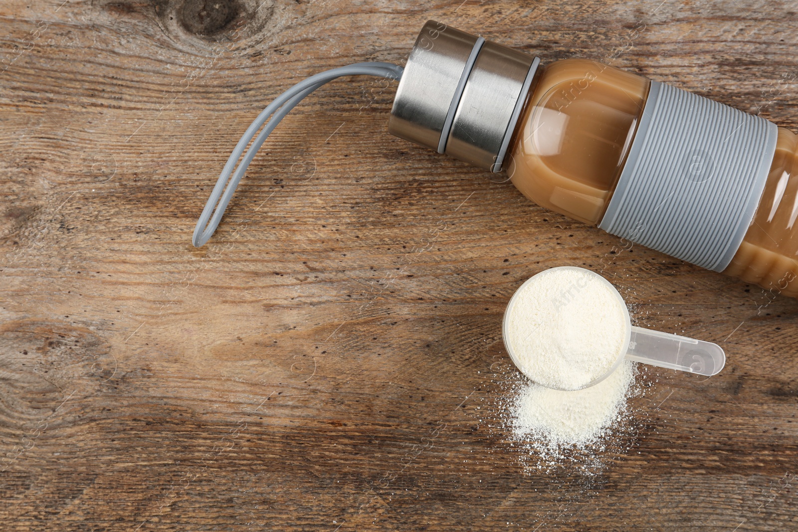 Photo of Measuring scoop of protein powder and bottle with shake on wooden table, flat lay. Space for text