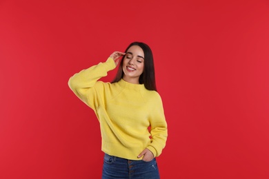 Beautiful young woman wearing yellow warm sweater on red background