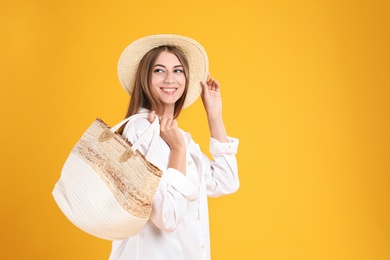 Photo of Beautiful young woman with stylish straw bag on yellow background. Space for text