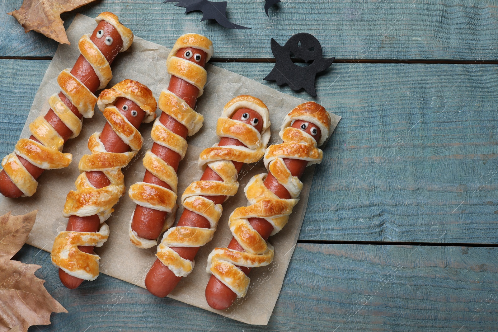 Photo of Cute sausage mummies served on blue wooden table, flat lay with space for text. Halloween party food