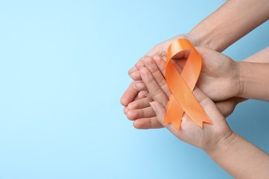 Couple holding orange ribbon on light blue background, top view with space for text. Multiple sclerosis awareness