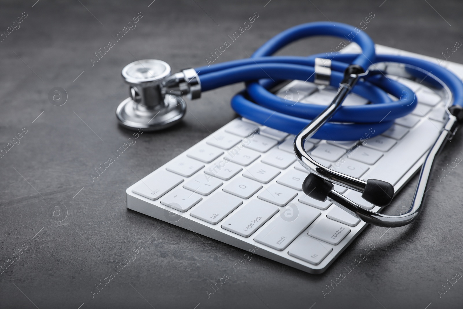 Photo of Computer keyboard with stethoscope on grey table, closeup