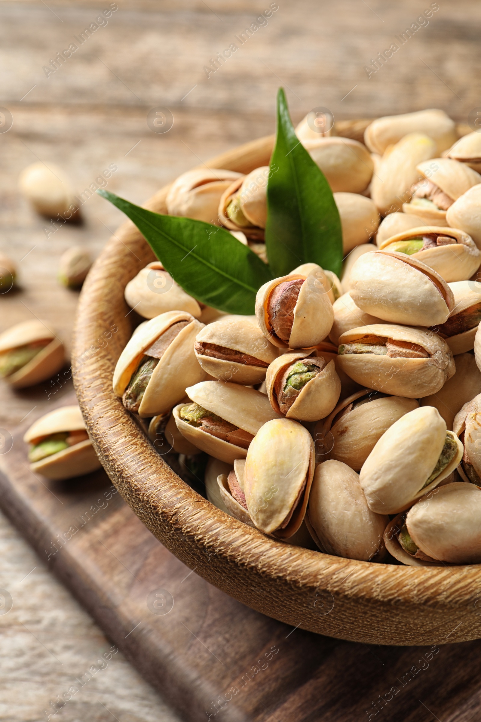 Photo of Organic pistachio nuts in bowl on wooden table, closeup