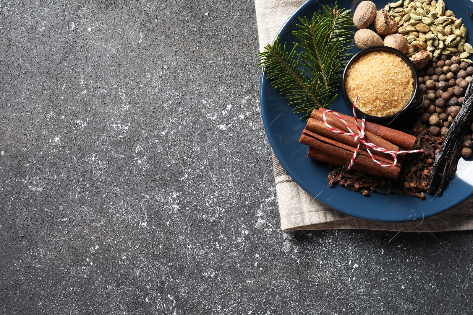 Photo of Different aromatic spices and fir branches on grey textured table, top view. Space for text