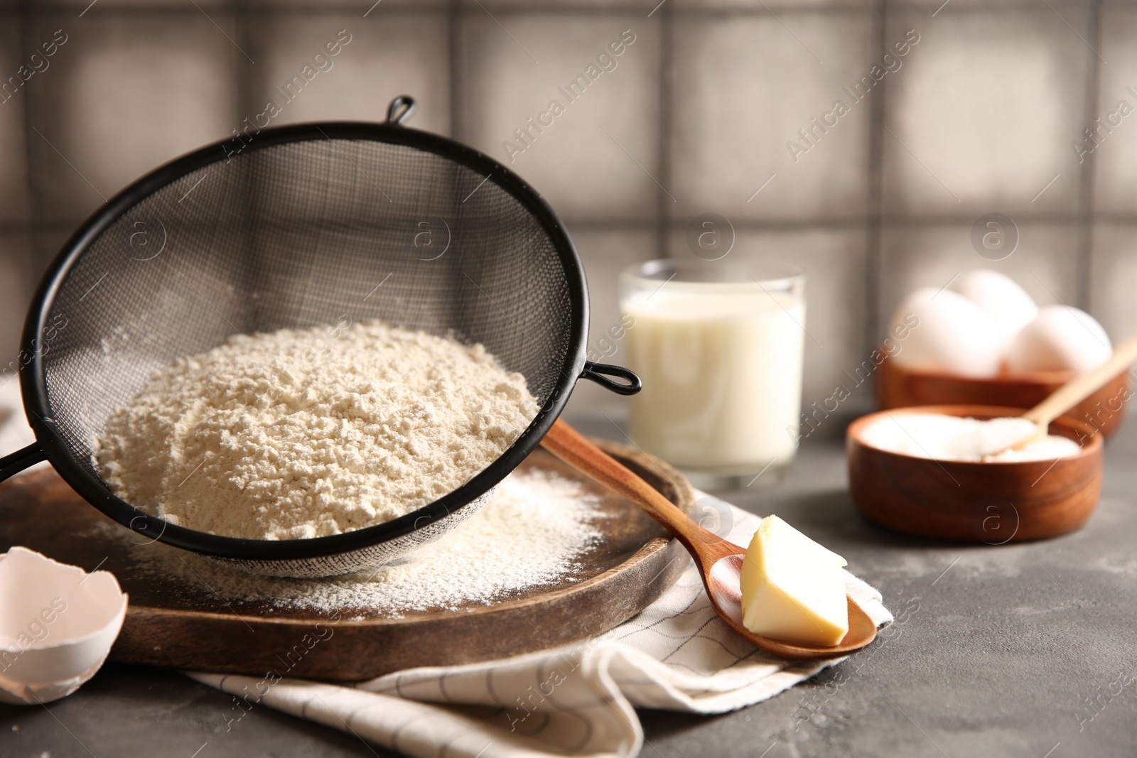 Photo of Making dough. Flour in sieve, spoon and butter on grey textured table, closeup