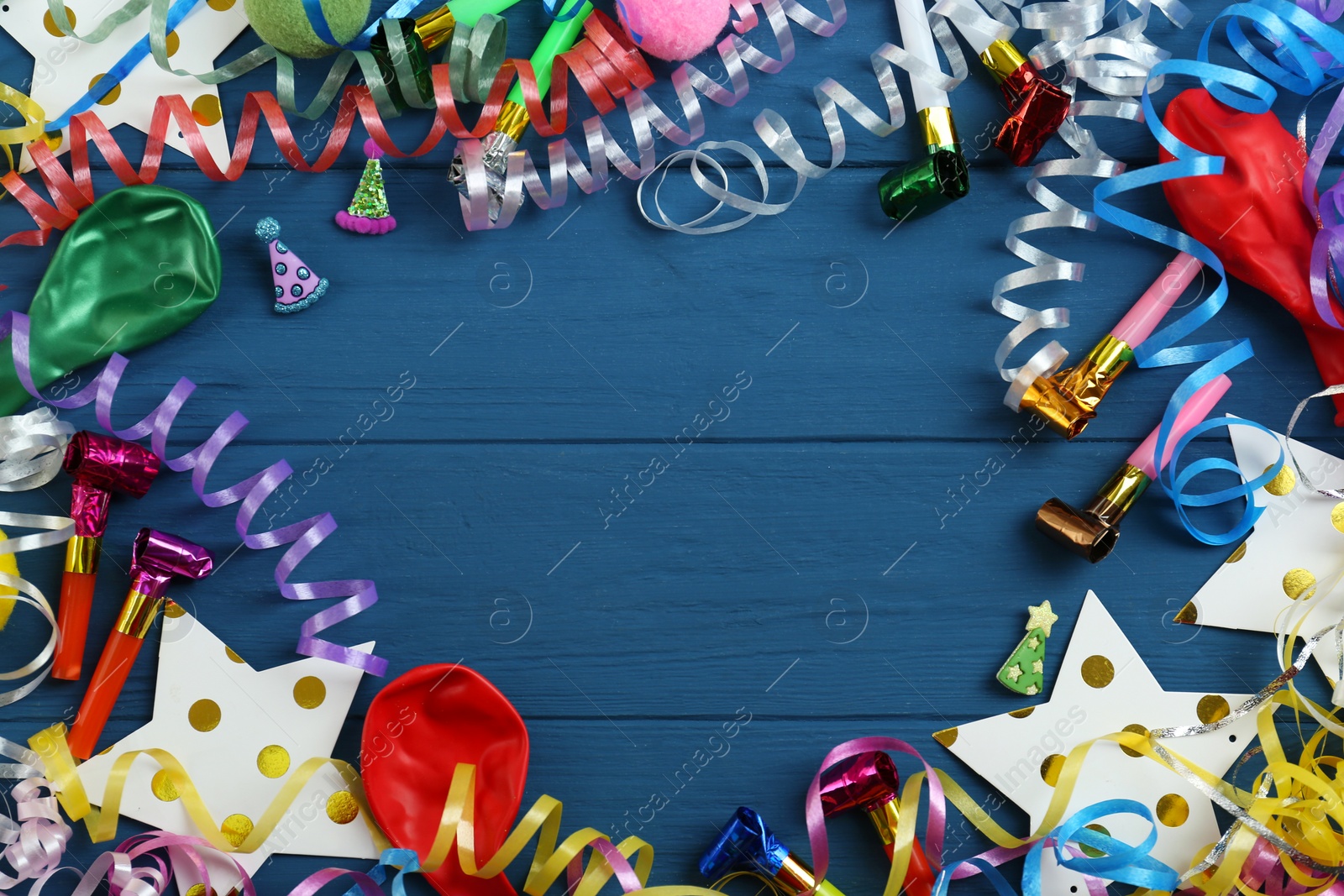 Photo of Frame of colorful serpentine streamers and other party accessories on blue wooden background, flat lay. Space for text