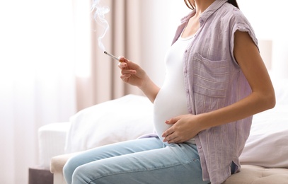 Photo of Young pregnant woman smoking cigarette at home, closeup