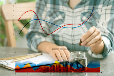 Image of Finance trading concept. Woman putting coins into jar at table and charts, closeup