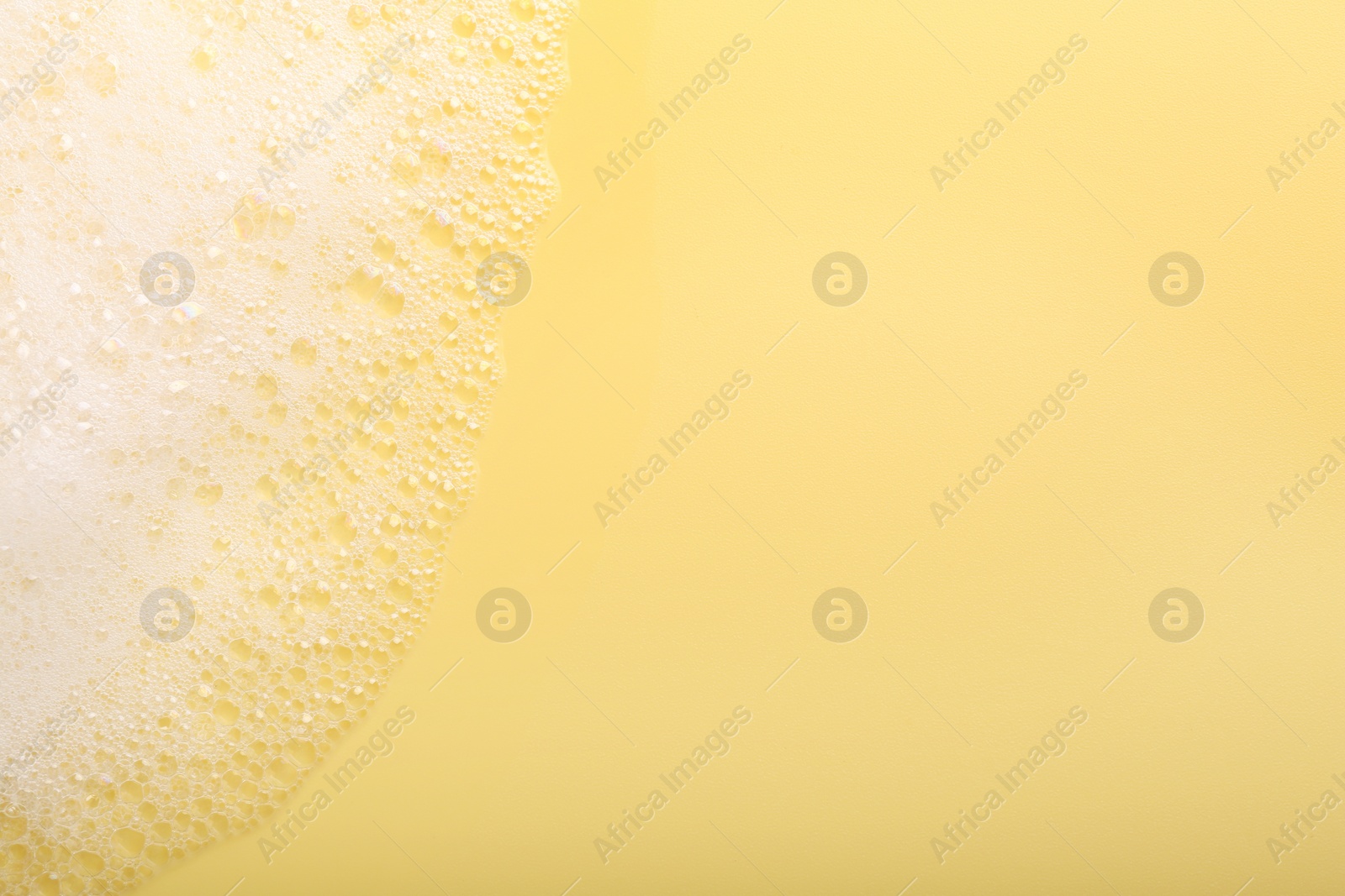 Photo of White fluffy foam on yellow background, top view. Space for text