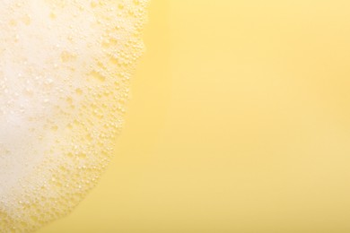 Photo of White fluffy foam on yellow background, top view. Space for text