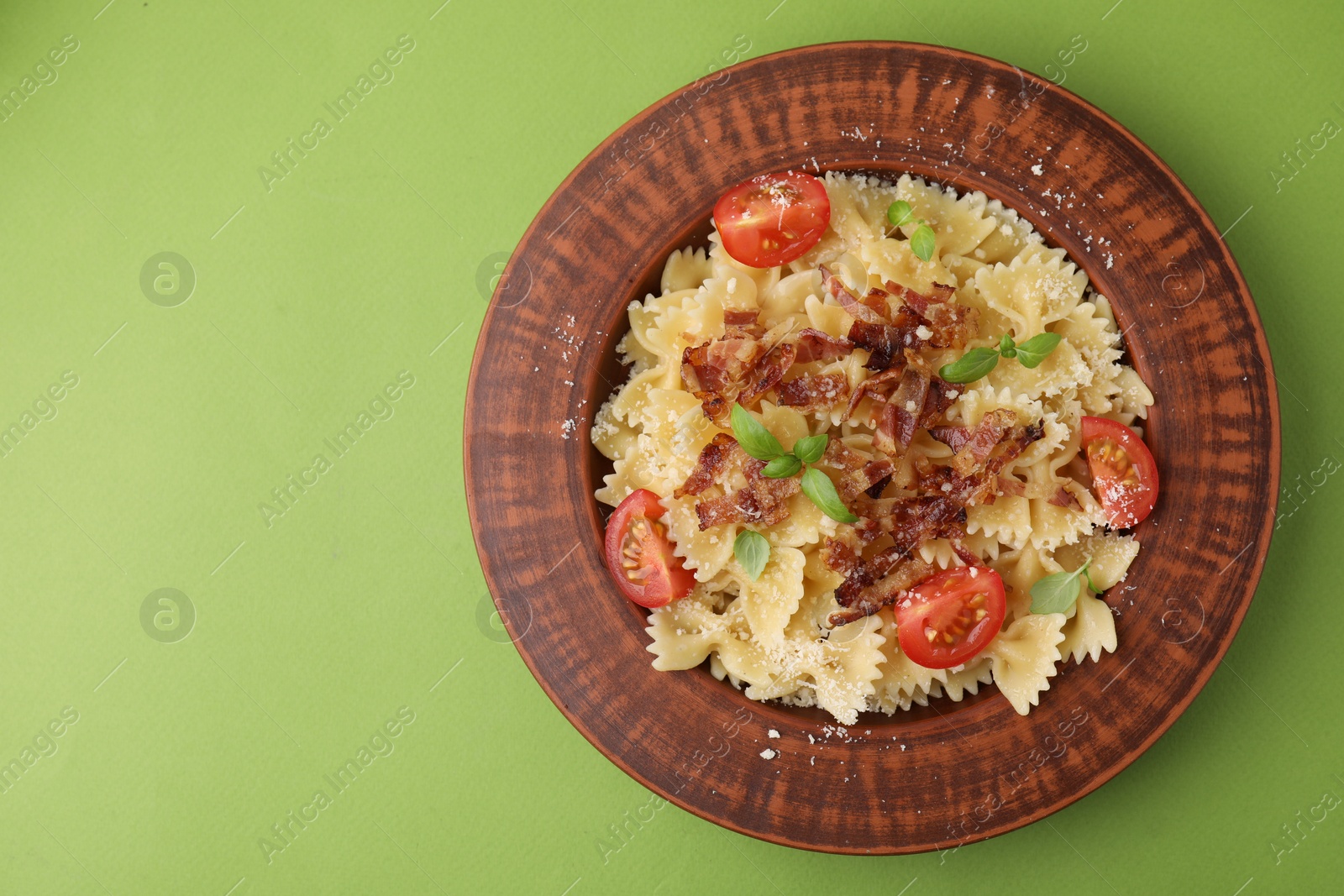 Photo of Tasty pasta with bacon, tomatoes and basil on light green table, top view. Space for text