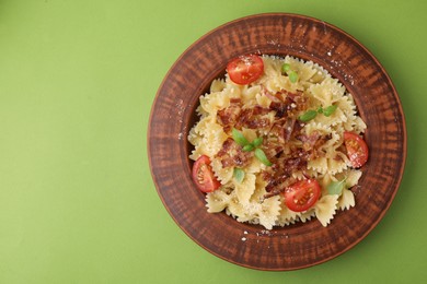 Tasty pasta with bacon, tomatoes and basil on light green table, top view. Space for text