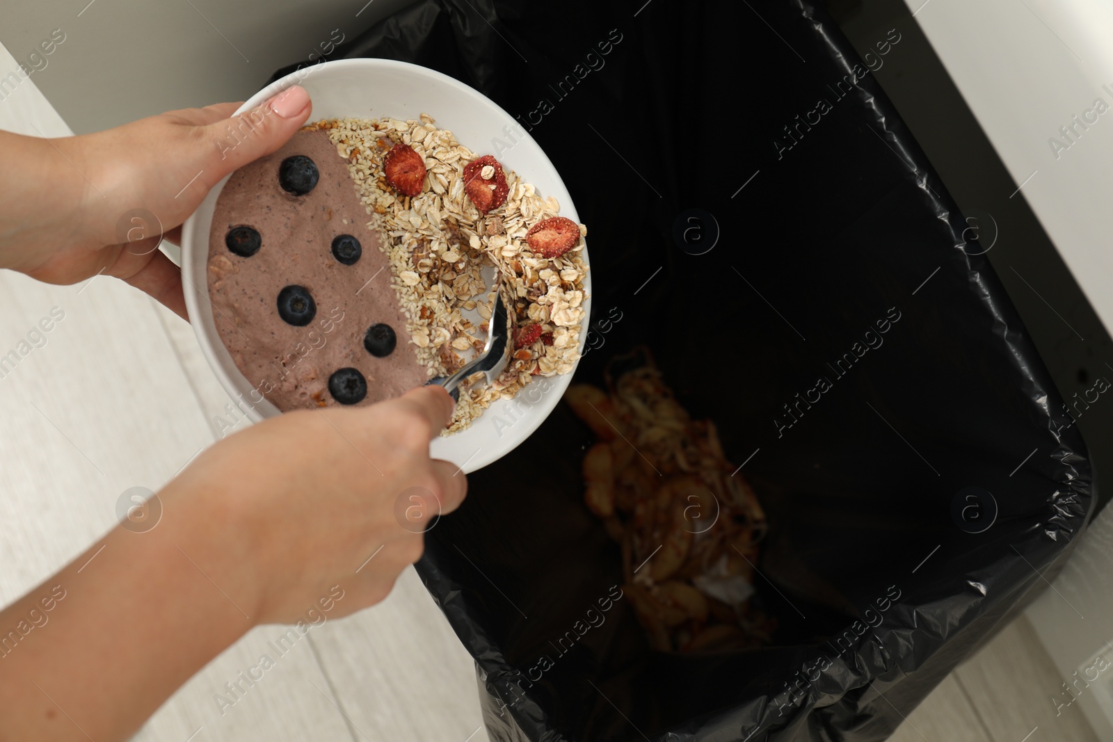 Photo of Woman throwing oatmeal with berries into bin indoors, top view