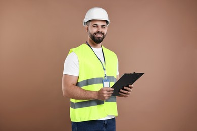 Engineer in hard hat holding clipboard on brown background