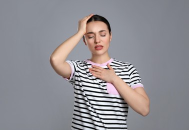 Young woman suffering from cold on grey background