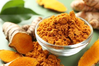 Photo of Aromatic turmeric powder and raw roots on green background, closeup