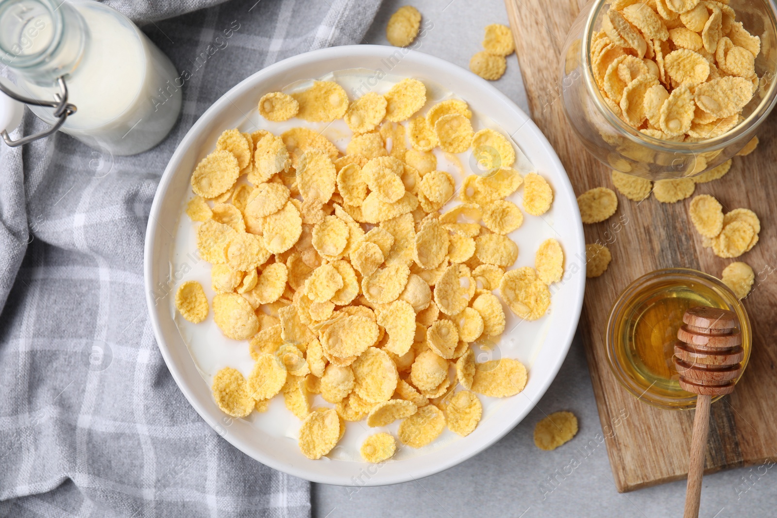 Photo of Breakfast cereal. Corn flakes and milk in bowl on light grey table, flat lay