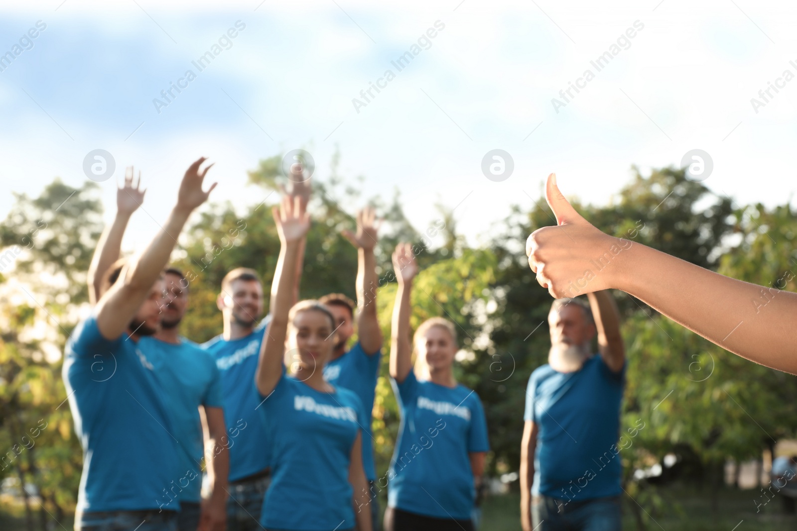 Photo of Woman showing thumb up at volunteers meeting. Group of people outdoors