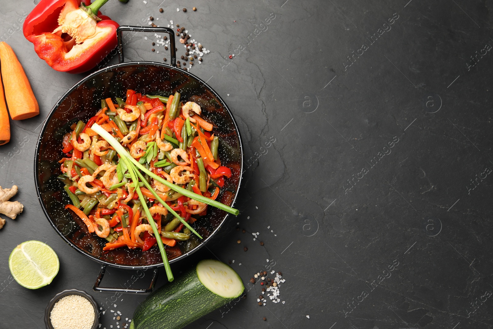 Photo of Shrimp stir fry with vegetables in wok and ingredients on black table, flat lay. Space for text