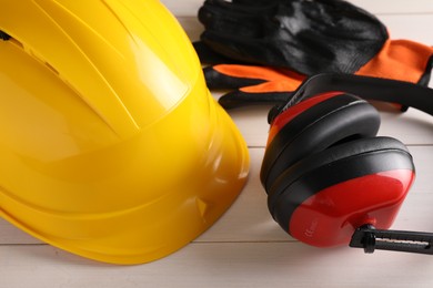 Photo of Hard hat, earmuffs and gloves on white wooden table, closeup. Safety equipment