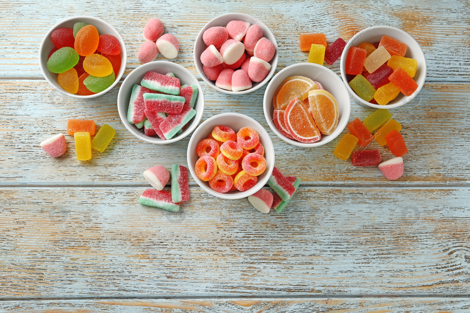 Photo of Flat lay composition with bowls of different jelly candies on wooden background. Space for text