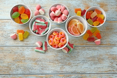Flat lay composition with bowls of different jelly candies on wooden background. Space for text
