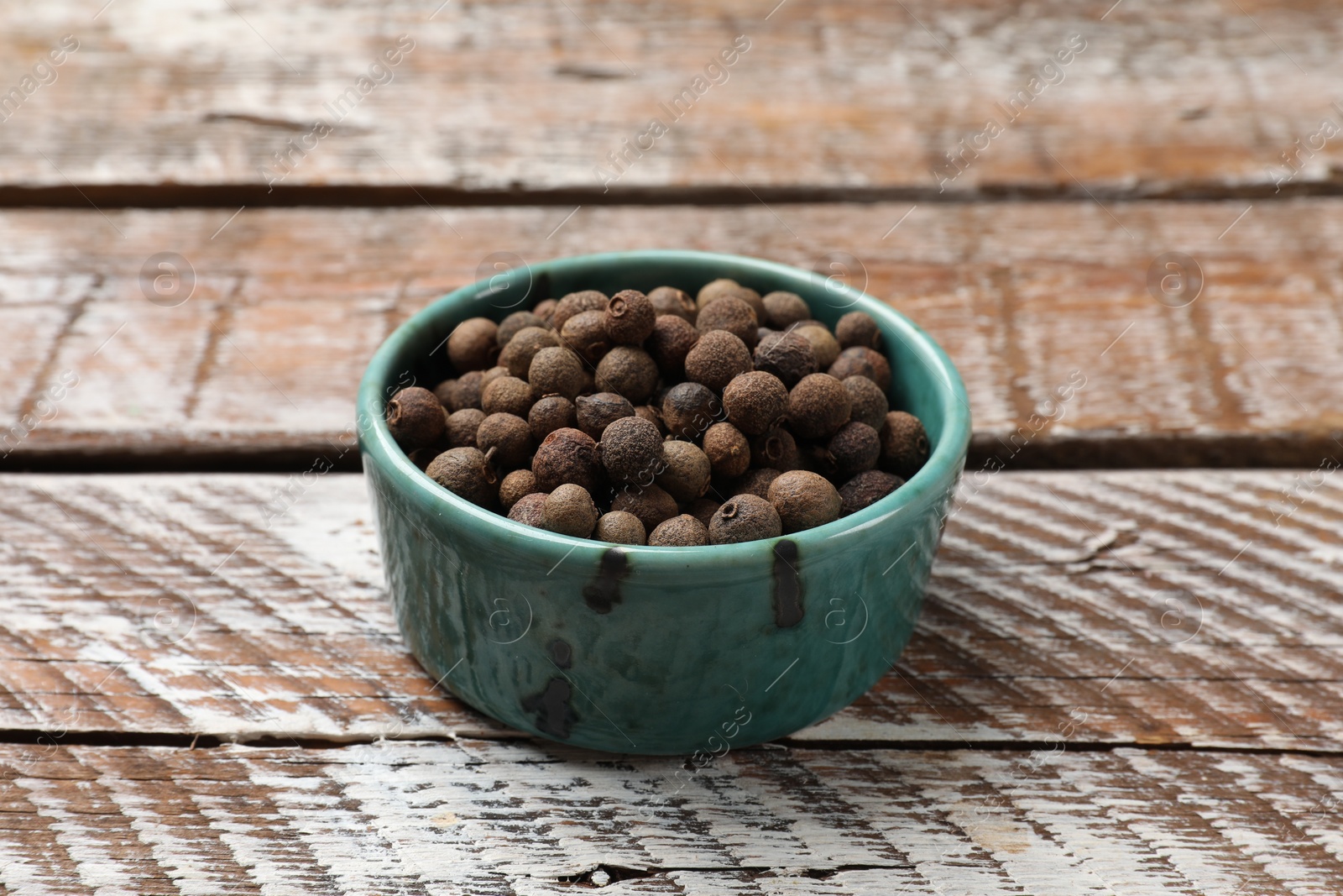 Photo of Aromatic allspice pepper grains in bowl on wooden table