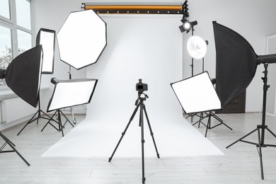 Tripod with camera and professional lighting equipment in modern photo studio