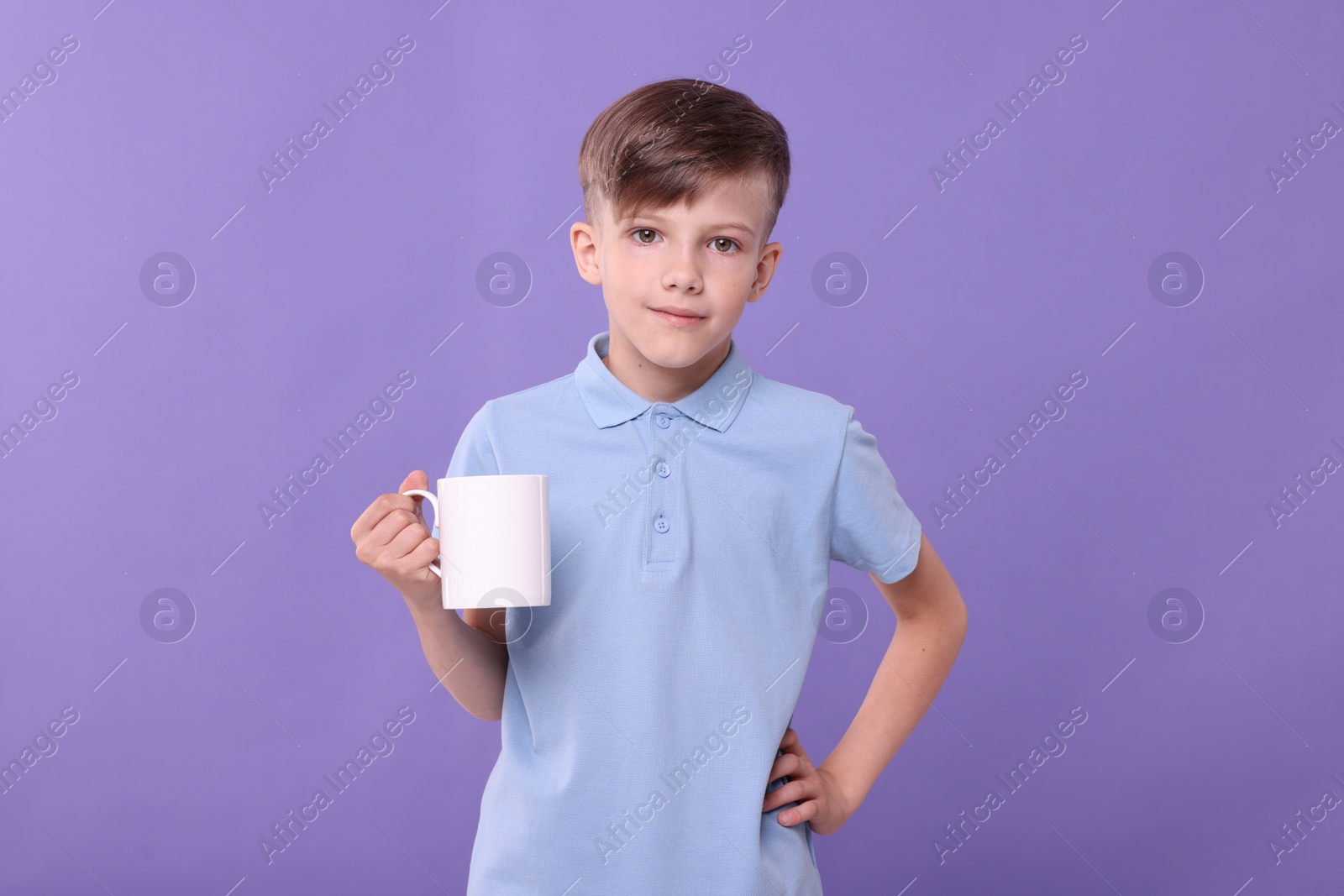 Photo of Cute boy with white ceramic mug on violet background