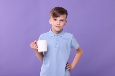 Cute boy with white ceramic mug on violet background