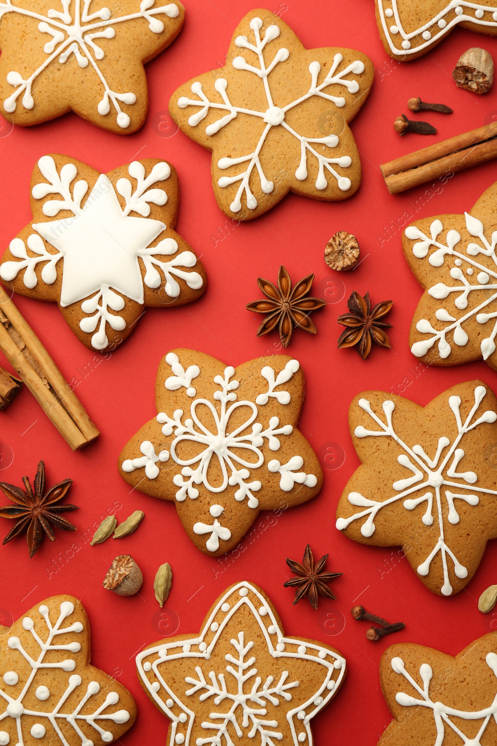 Photo of Tasty star shaped Christmas cookies with icing and spices on red background, flat lay