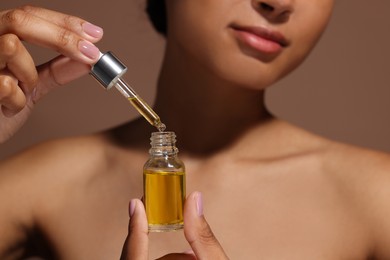 Photo of Woman with bottle of serum and dropper on brown background, closeup