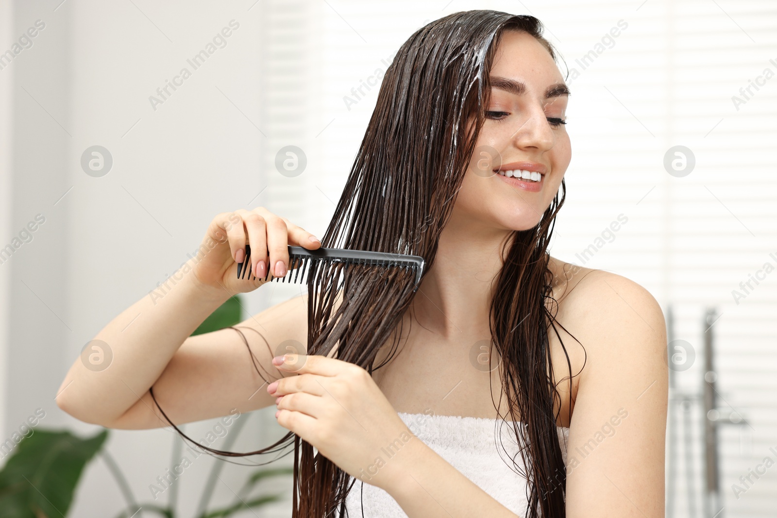 Photo of Young woman brushing hair after applying mask in bathroom