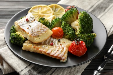 Photo of Tasty cod cooked with vegetables served on table, closeup