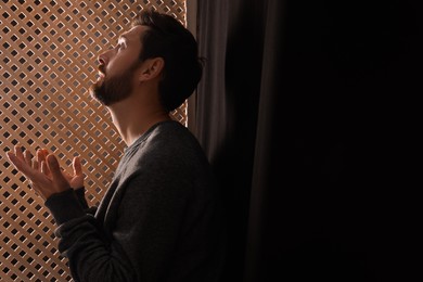 Photo of Man praying to God during confession in booth, space for text