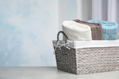 Basket with soft bath towels on table against blurred background. Space for text