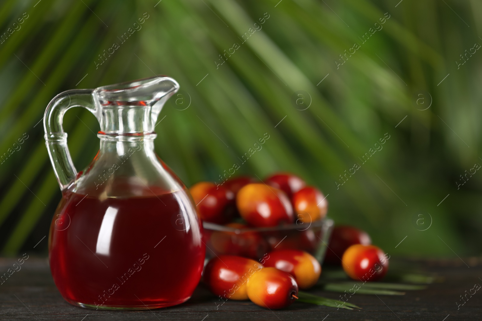 Image of Palm oil in glass jug, tropical leaf and fruits on wooden table. Space for text