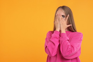 Embarrassed woman covering face with hands on orange background, space for text