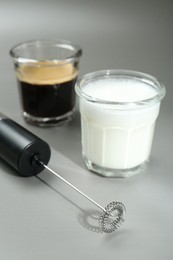 Mini mixer (milk frother), whipped milk and coffee in glasses on grey background