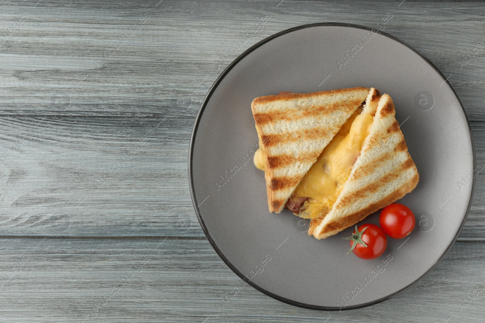 Photo of Tasty sandwiches with ham, melted cheese and tomatoes on grey wooden table, top view. Space for text