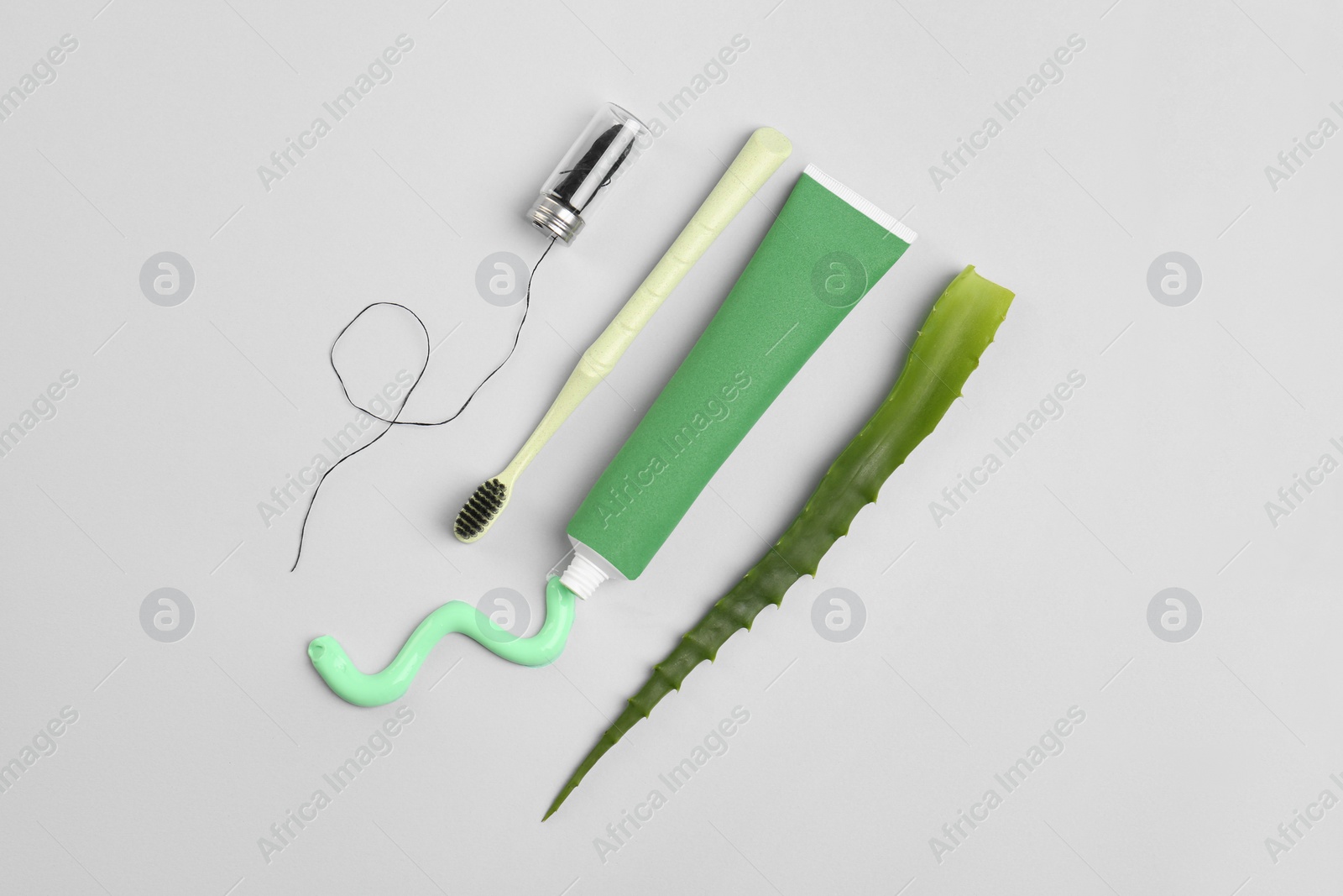 Photo of Tube of toothpaste, toothbrush, dental floss and fresh aloe on light grey background, flat lay