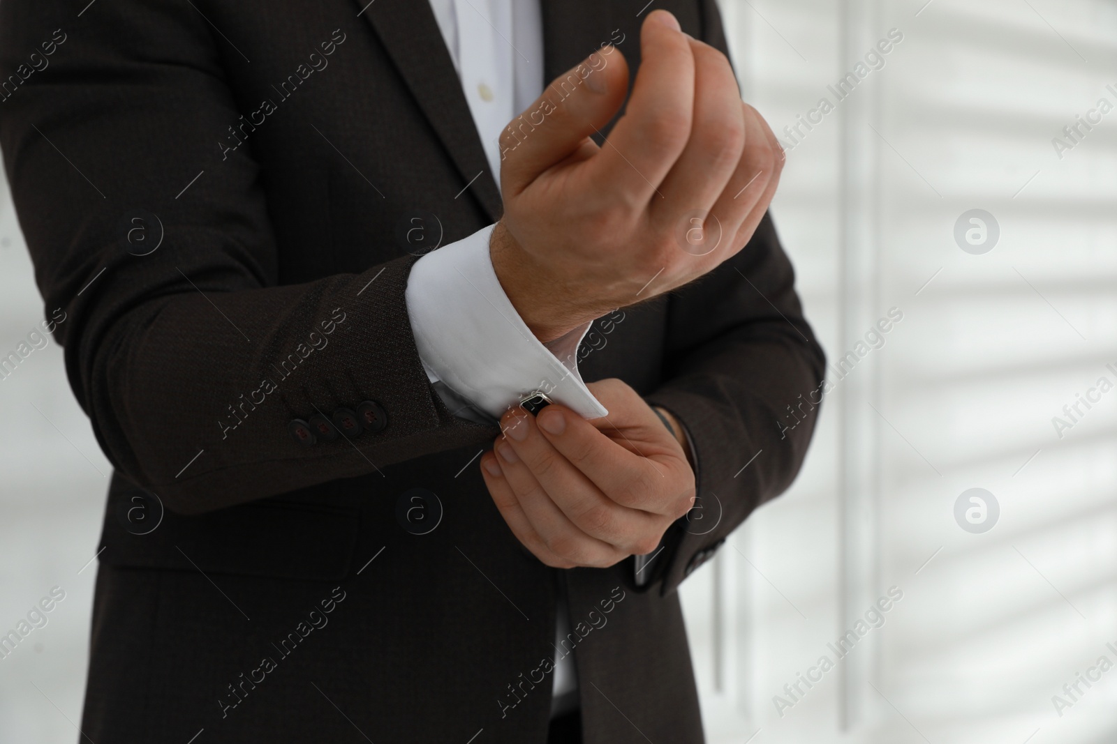 Photo of Man wearing stylish suit and cufflinks near white wall, closeup