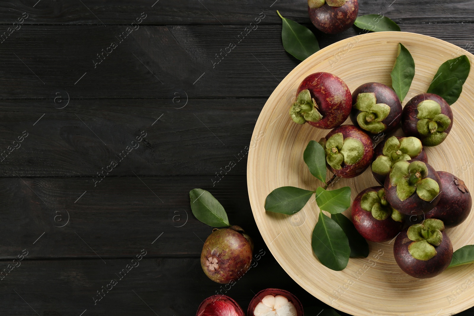 Photo of Fresh ripe mangosteen fruits on dark wooden table, flat lay. Space for text